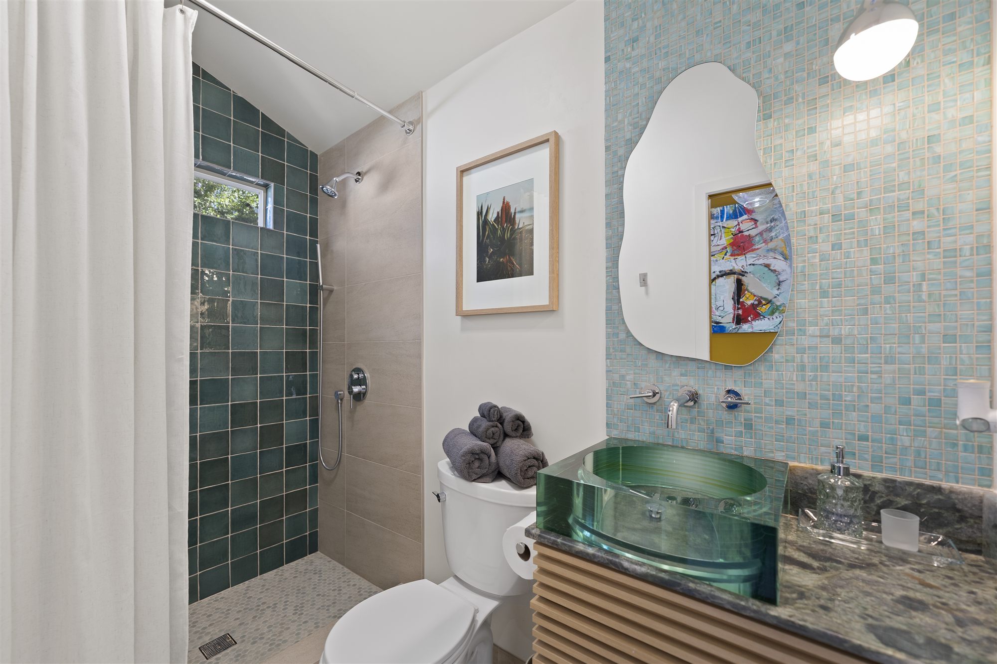 Bathroom with green tile shower, glass vessel sink and wavy mirror