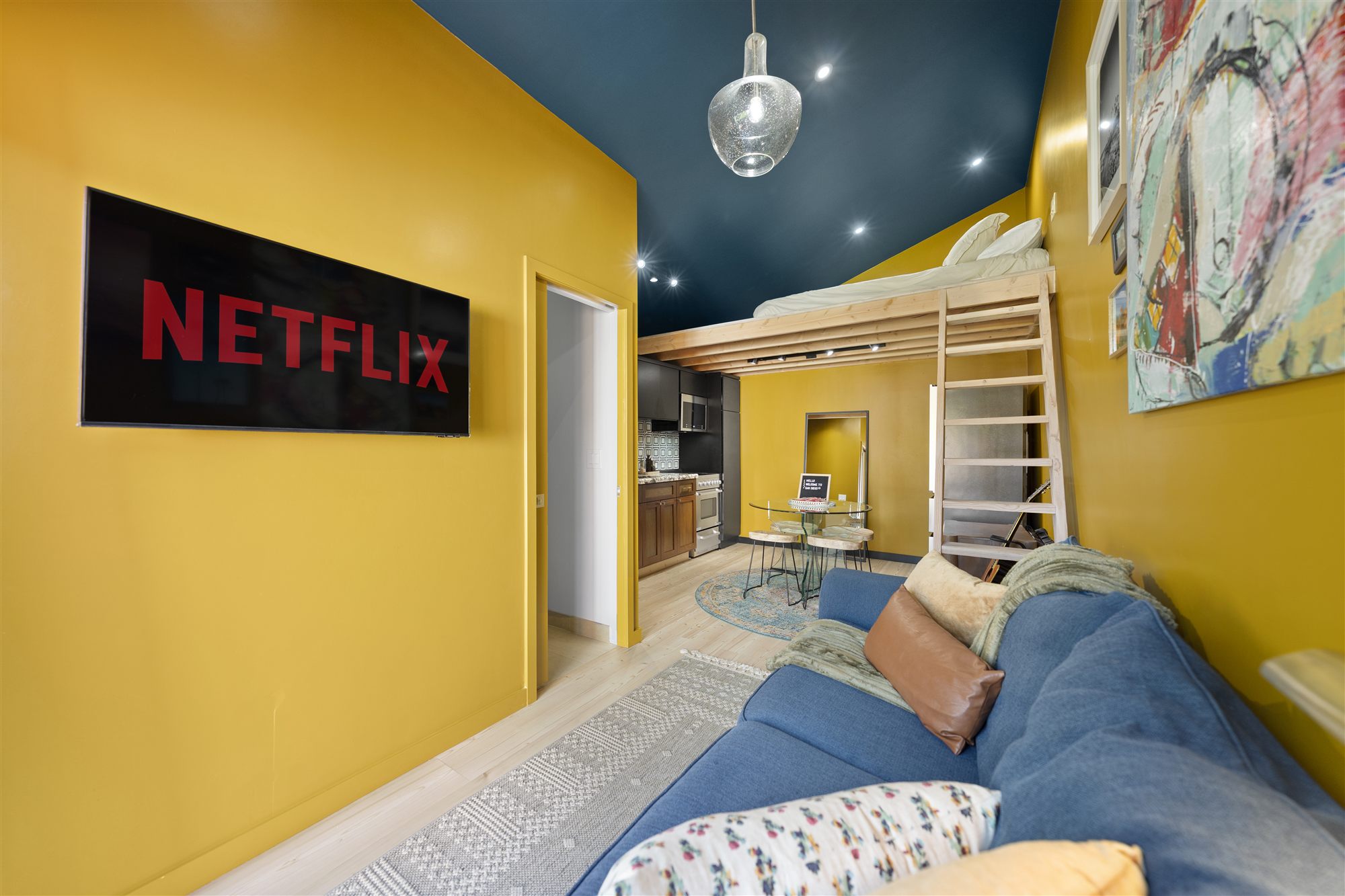 Living room with Netflix on the wall-mounted TV, loft ladder, mustard walls and navy ceiling