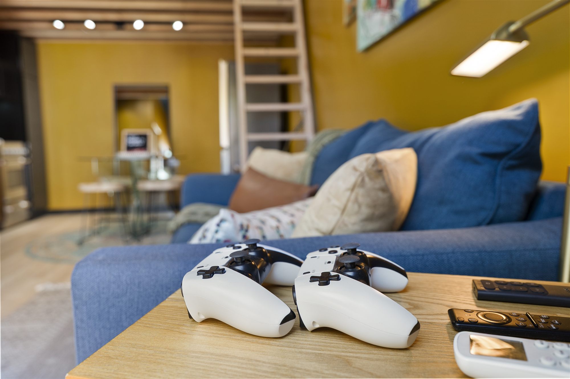 PS5 controllers on the coffee table with sofa and loft ladder soft-focus behind
