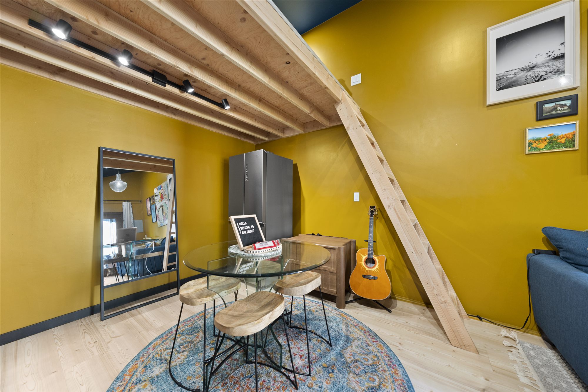 Round glass dining table with live-edge stools, guitar against the wall, loft ladder behind